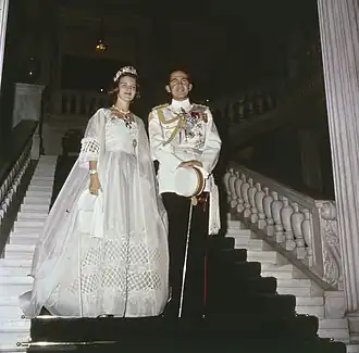 Photographie en couleur montrant une femme portant une robe et un homme en uniforme de marine dans un escalier.