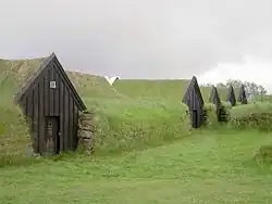 Photographie de maisons islandaises médiévales, en bois, incrustées dans des mottes de terre.