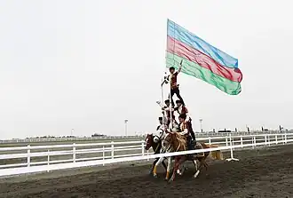 Trois chevaux montés au galop par cinq cavaliers voltigeurs sont un au centre déploie le drapeau de l'Azerbaïdjan