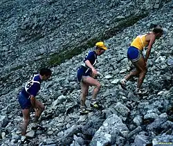 Trois coureurs grimpant dans un pierrier, les mains posées sur les cuisses.