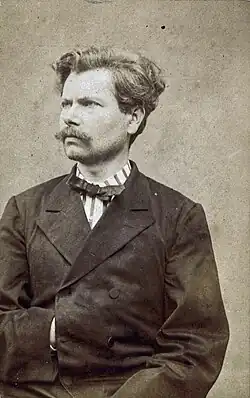 Portrait en photographie sépia d'un homme portant veste et nœud papillon. L'homme regarde vers la droite, et glisse sa main droite sous sa veste.