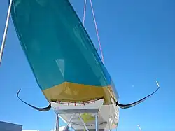 Vue du dessous du bateau, depuis l'avant, en contre-plongée. Les foils se détachent sur le ciel.