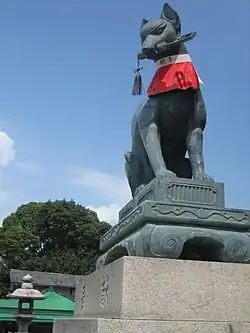 Un renard-gardien (狛狐, komakitsune?) en face d'un Inari-jinja avec une clef dans la gueule.