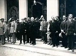 Photographie noir et blanc. Sur un perron une assemblée de personnages, du début du XXe&nbsp;siècle, en tenue de ville pose.