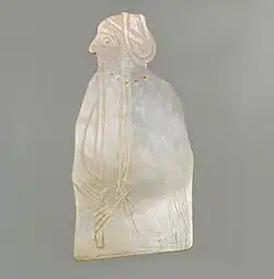 Élément en nacre gravé représentant une femme portant une flûte et un pendentif en forme de sceau-cylindre.
