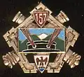 Deux canons croisés, chargés d'un pentagone fortifié, chargé au centre d'un rectangle portant, dans une paysage montagneux, une tourelle tirant avec ses deux canons de face. En pointe, un écusson avec les armes de Nice et en chef un écusson avec le numéro 158.