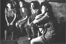 Image en noir et blanc de quatre femmes en attente, assises en ligne contre un mur en train de discuter.