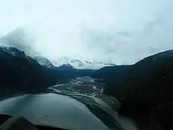 Vue aérienne d'une vallée fluviale avec des montagnes glaciaires en arrière-plan.