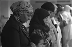 Photographie en noir et blanc d'une rangée de femmes en prière, les yeux fermés, la tête baissée et les bras croisés.