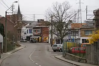 Photographie d'un village, au centre-gauche, une route, au milieu une place, au fond une église.