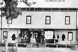 Une photographie ancienne d'un bâtiment portant les inscriptions « Canada », « J. M. Hill » et « U.S.A. ».