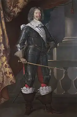 Debout, en armure, bâton à la main, larges bottes.