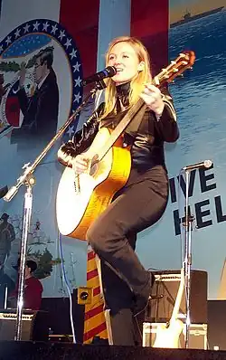 Une femme blonde chantant et portant une guitare sur scène.