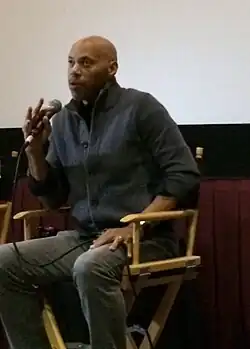 Pendant une conférence de presse, Ridley est assis et parle dans un micro.