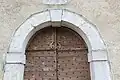 Détail du portail avec sa porte en bois cloutée et sculptée. À gauche et à droite, deux pierres sculptées indiquent la date de construction et l'initiale de bienfaiteurs 16M et B87.