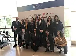Photo en couleurs d'un groupe de 9 femmes et 3 hommes posant devant un panneau de logos d'entreprises.