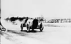 Photo de Jules Goux franchissant recevant à vive allure le drapeau à damier des 500 miles d'Indianapolis 1913.