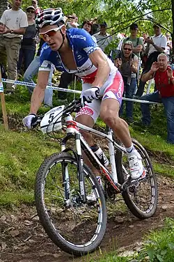 Homme descendant une pente à VTT, portant une tenue bleu-blanc-rouge.