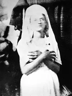 photographie noir et blanc d'une jeune femme très pâle, les bras croisés sur la poitrine