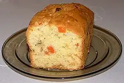 Photographie couleur d'un gâteau coupé en deux de forme rectangulaire et garni de petits éclats de fruits colorés.