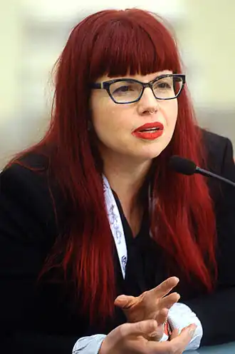 femme à lunettes, cheveux roux, habillée en noir.