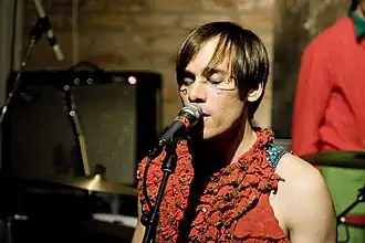 Chanteur devant un micro, des instruments dans le fond.