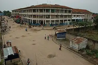Un grand bâtiment fait l'angle devant un croisement de rues. Des petits bâtiments en tôle sont présents le long des rues.