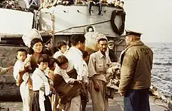 Photographie d'une groupe d'une dizaine de réfugiés, la plupart enfants, sur le pont d'un bateau américain.