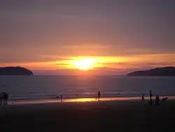 Photographie d'un coucher de soleil sur une place. De part et d'autre de l’horizon se trouvent deux îles.