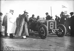 Photo de deux hommes en tenue de pilote dans une voiture prête à prendre le départ d'une course devant des officiels.