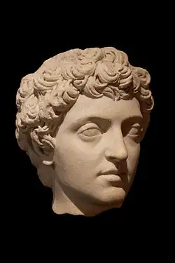 Sur fond noir, tête aux cheveux courts bouclés du jeune homme délicatement éclairée, en marbre teinte d'abricot clair.