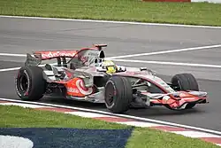 Photographie d'une monoplace de Formule grise et rouge, vue de trois-quarts, près d'un vibreur.