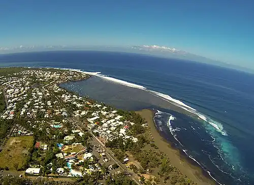 Une plage de sable noir, où une pointe de récif fait naître d'importantes vagues, propices au surf.