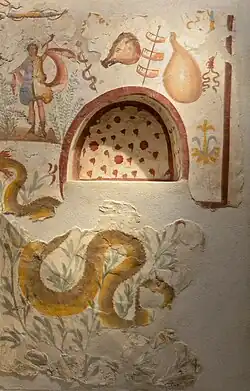 Photographie couleur. Mur orné d'une fresque colorée en nuances d'ocre sur lequel se trouve une niche voutée.