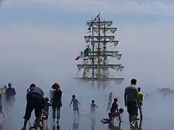 Photographie du miroir d'eau avec, en arrière plan, le mât d'un bateau à voile.