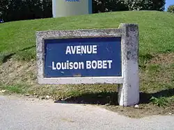 Photographie d'un panneau de rue avec des écritures blanches sur fond bleu.