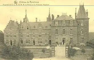 Photo en noir et blanc d'un large château de style mosan avec de nombreuses toitures devant une pelouse.