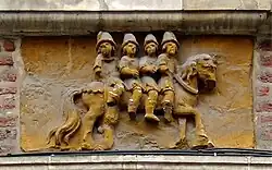 Plaque gravée dans la pierre, et en partie endommagée, placée au-dessus d'une devanture et représentant quatre hommes sur un même cheval