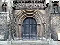 Un portail roman normand subsistant, délicatement sculpté, surmonté par une galerie des rois gothique.