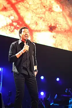 un chanteur,chemise et pantalon sombre,sur scène avec un microphone