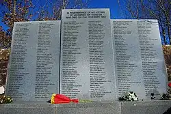 Photo d'un mémorial comportant trois parties en pierres grises. Une partie du milieu et deux parties sur les côtés, qui sont légèrement moins hautes. Sur l'ensemble se trouve des inscriptions écrites en noires.