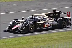 Photographie d'un prototype d'endurance noir et or, vu de trois-quarts, avec le numéro 12 sur son flanc.