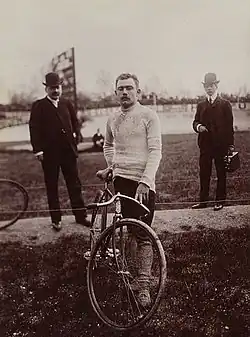 Photographie en noir et blanc d'un cycliste se tenant debout à côté de son vélo.