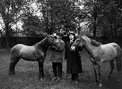 Photographie en noir et blanc de deux hommes dont un militaire, entourés de deux petits chevaux.