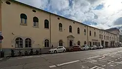 Photo d'un bâtiment allongé en crépi beige à un étage, avec des fenêtres plein cintre.