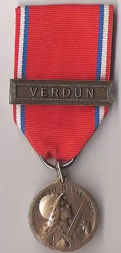 Médaille métallique ronde suspendue à un ruban rouge.