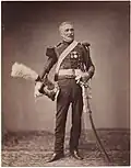 Photographie d'un ancien soldat de Napoléon, tenant sa coiffe sur le côté.