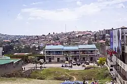 Vue depuis une colline sur une rue animée avec un immeuble de deux étages et une station-service. En arrière-plan, une colline de la ville construite avec des maisons.