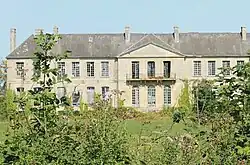 Vue d'un grand bâtiment abandonné avec des hautes herbes au premier plan
