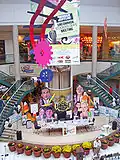 Photo d'intérieur d'un centre commercial présentant une exposition avec des affiches de la série et des fabrications en papier des personnages.